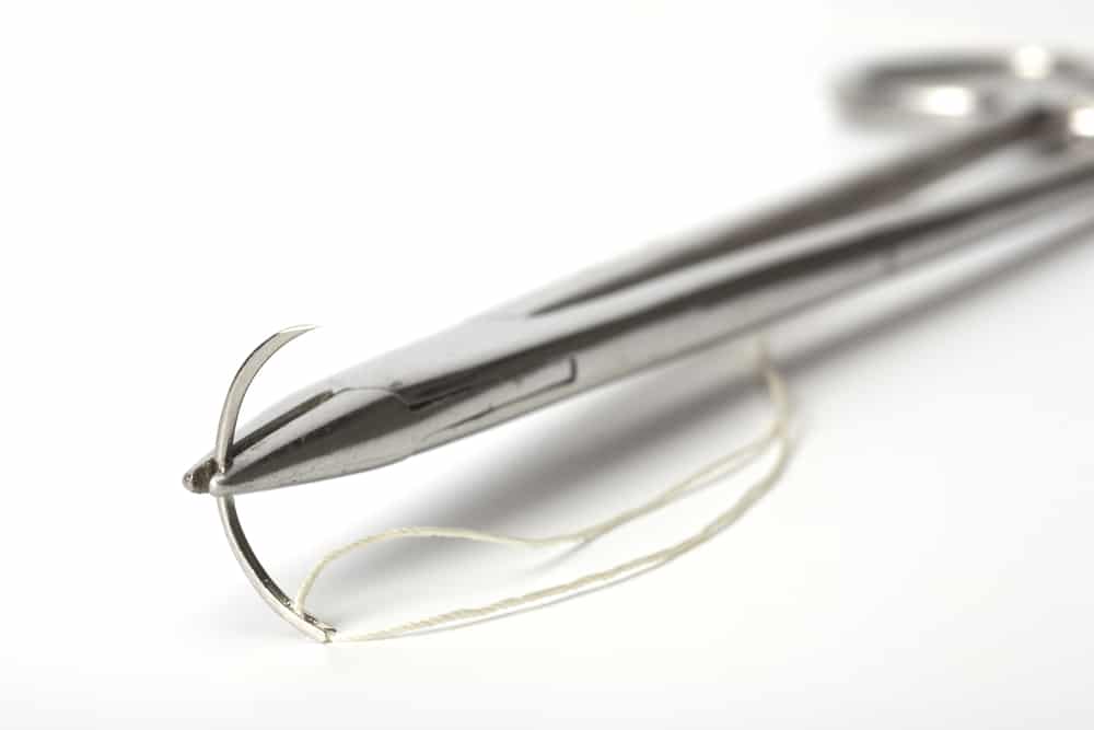 The old holder  with a surgical needle and silk. On a white background.